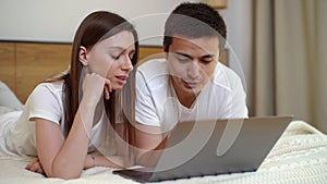 Young couple relaxing in bed with laptop. Lying together in bright bedroom