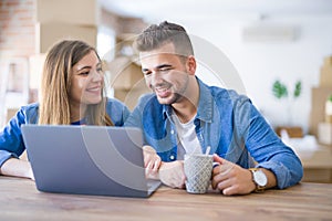 Young couple relaxing drinking a coffee and using the computer laptop around cardboard boxes, very happy moving to a new house