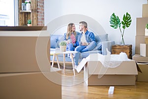 Young couple relaxing drinking a cup of coffee sitting at sofa of  new home with cardboard boxes around them, very happy moving to