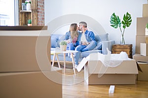 Young couple relaxing drinking a cup of coffee sitting at sofa of  new home with cardboard boxes around them, very happy moving to