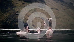 Young couple relaxing in hot springs in Iceland. Traveling man and woman swimming in mountains valley, romantic date.