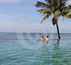 Young couple relaxing in infinity pool under coco palms