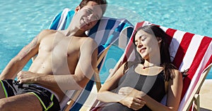 Young couple relaxing poolside in deck chairs