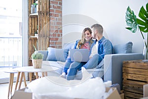 Young couple relaxing sitting on the sofa using the computer laptop around cardboard boxes, very happy moving to a new house