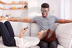 Young Couple Relaxing On Sofa At Home Looking At Mobile Phone Together