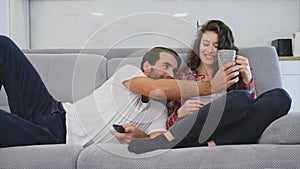 Young couple relaxing in their apartment, lying on the couch and watching the movie.