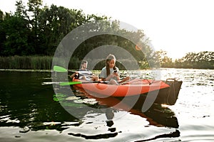 Young couple relaxing together, kayaking on the river. Woman using her smartphone while resting