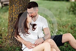 Young couple relaxing under tree in park on sunny day. Happy couple in love spend time outdoors together. Handsome man and pretty