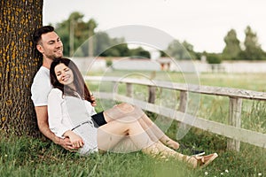 Young couple relaxing under tree in park on sunny day. Happy couple in love spend time outdoors together. Handsome man and pretty