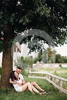 Young couple relaxing under tree in park on sunny day. Happy couple in love spend time outdoors together. Handsome man and pretty