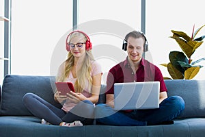 Young couple relaxing using laptop and tablet on sofa