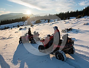 Young couple riders on four-wheelers ATV bikes on snow, enjoying sunset in the the mountains in winter