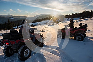 Young couple riders on off-road quad bikes, enjoying beautiful sunset in the the mountains in winter