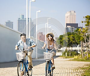 young couple riding on bicycle in city park
