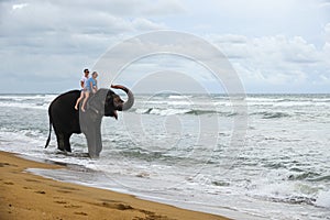 Young couple is riding on an elephant with trunk up on the background of a tropical ocean beach