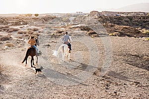 Young couple riding horses doing excursion with dog pets at sunset - Main focus on woman back