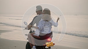 Young couple riding motorcycle on ocean beach at sunrise. Man, woman travelling by motor bike on coastline along sea