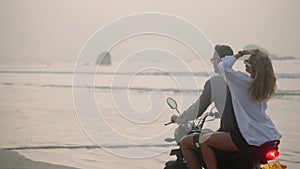 Young couple riding motorcycle on ocean beach at sunset. Man, woman travelling by motor bike on coastline along sea