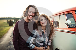 A young couple on a roadtrip through countryside, standing by minivan.