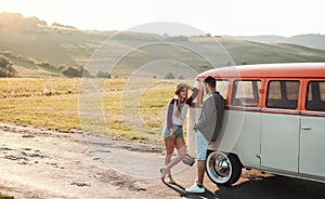 A young couple on a roadtrip through countryside, standing by minivan.