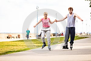 Young couple rollerblading in park holding hands