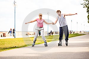 Young couple rollerblading in park holding hands.