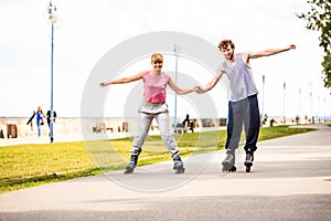 Young couple rollerblading in park holding hands.