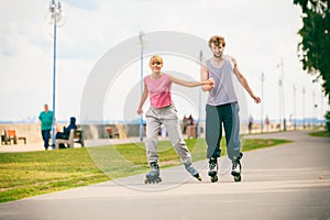 Young couple rollerblading in park holding hands.