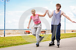 Young couple rollerblading in park holding hands.