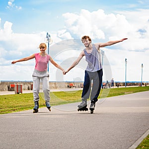 Young couple rollerblading in park holding hands.