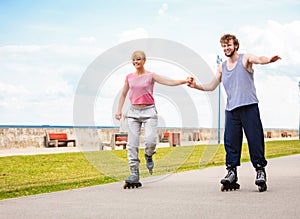 Young couple rollerblading in park holding hands.