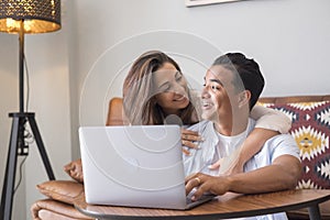 Young couple romancing while working on laptop at home. Woman embracing her husband while he is using laptop in living room. Happy