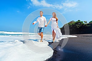 Young couple run by black sand beach along sea surf