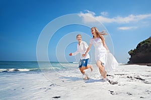 Young couple run by black sand beach along sea surf
