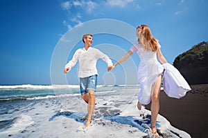 Young couple run by black sand beach along sea surf