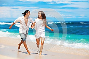 Young couple run by white sand beach along sea surf