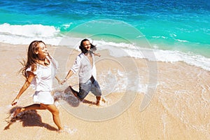 Young couple run by white sand beach along sea surf