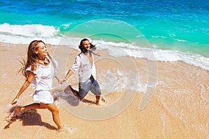 Young couple run by white sand beach along sea surf