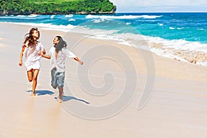 Young couple run by white sand beach along sea surf