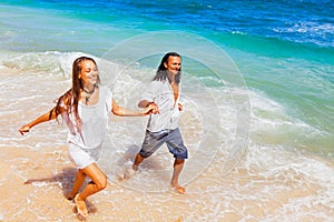 Young couple run by white sand beach along sea surf