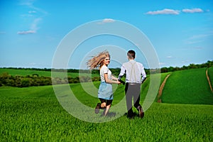 Young couple running along a green field on a lovely sunny day