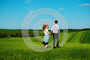 Young couple running along a green field on a lovely sunny day