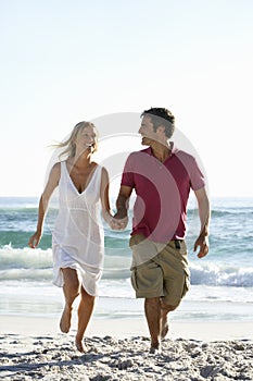 Young Couple Running Along Sandy Beach On Holiday