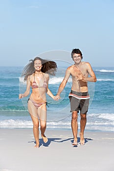 Young Couple Running On Beach Wearing Swimwear