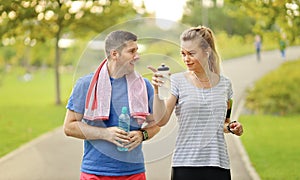 Young couple running and chatting in city park. Cheerful caucasian modern man and woman in headsets jogging in nature and living