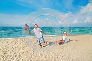 Young couple running at sea beach in santa hats with color sled