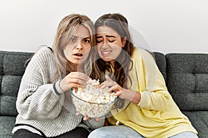 Young couple scared watching horror film eating popcorn at home