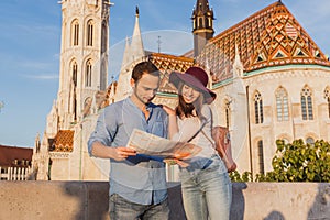 Young couple searching right direction on map from the point from Fisherman Bastion in Budapest with Matthias Church on