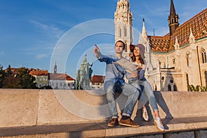 Young couple searching right direction on map from the point from Fisherman Bastion in Budapest with Matthias Church on