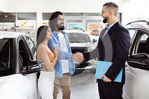 Young Couple Shaking Hands With Car Salesman at Dealership Showroom